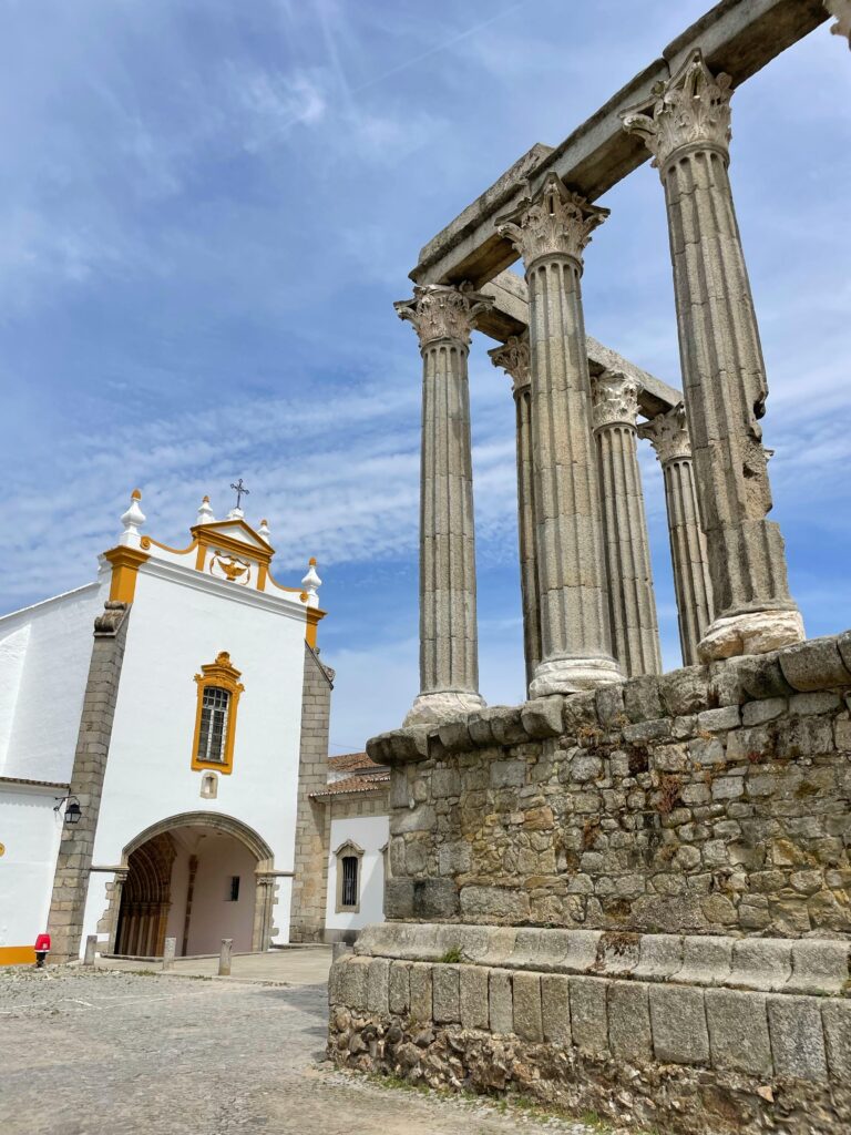 Explore the ancient Roman temple ruins and historic church in Évora, Portugal, under a bright blue sky.