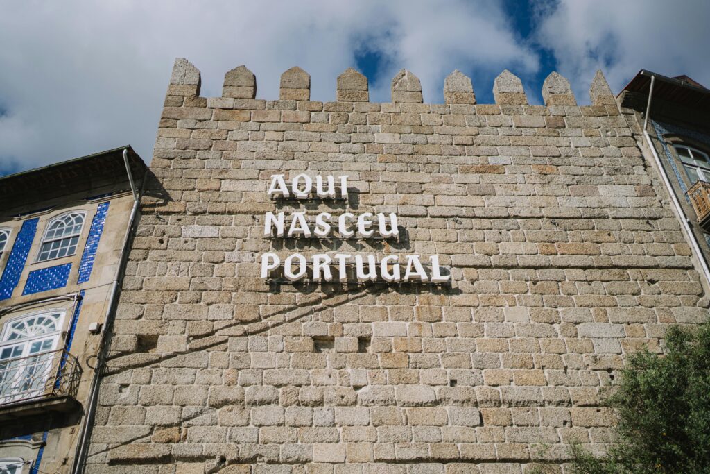 Medieval stone wall with 'Aqui Nasceu Portugal' sign in Guimarães under blue sky.